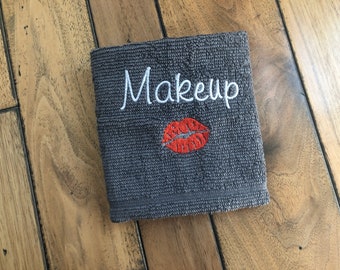Może przedstawiać: Szary ręcznik do rąk z haftowanym napisem "Makeup" w kolorze białym i haftowanym czerwonym odciskiem ust.
