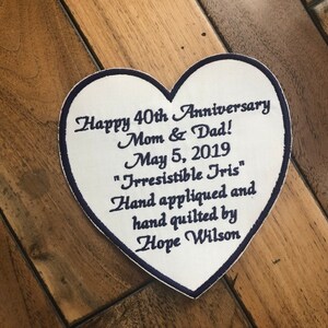 May include: White heart-shaped fabric patch with blue embroidered text: "Happy 40th Anniversary Mom & Dad! May 5, 2019 "Irresistible Tris" Hand appliqued and hand quilted by Hope Wilson"