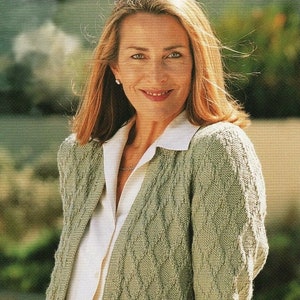 May include: A pale green open-front cardigan with a diamond pattern. The cardigan is worn over a white collared shirt and a brown skirt. The woman is smiling and wearing a ring on her finger.
