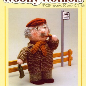 May include: Knitted doll pattern for a grandfather figure wearing a brown coat, orange scarf, and a red hat. The doll is holding a pipe and a green bag. The pattern is titled "Woolly Wotnots" and is numbered "N° 026 approx. 30 cm. (12") high".