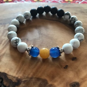 May include: A beaded bracelet with white, black, blue, and yellow beads. The bracelet has silver accents.