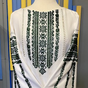 May include: White embroidered blouse with a green floral pattern. The embroidery is detailed and intricate, and the blouse has a classic, timeless style.