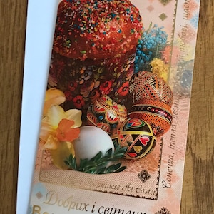 May include: A greeting card with a colorful Easter cake and decorated eggs. The card has a gold inscription that reads "Dobrix i svitlix Velikodnix Sviat!" which translates to "Happy and Bright Easter Holidays!"