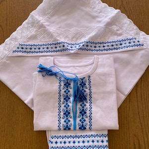 May include: A white embroidered baby outfit with blue and white embroidery. The outfit includes a shirt, pants, and a bonnet.