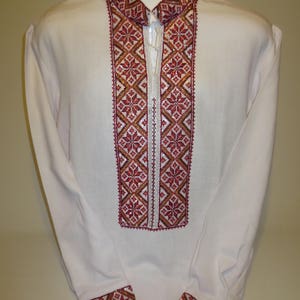 May include: A white long-sleeved shirt with red, gold, and white embroidered details on the collar and cuffs.
