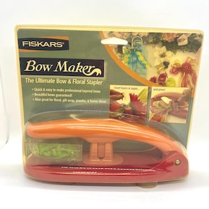May include: A Fiskars Bow Maker, the ultimate bow and floral stapler, packaged in a cardboard backing with product information and images. The tool is orange and red, featuring a stapling mechanism and a clear plastic compartment for staples.