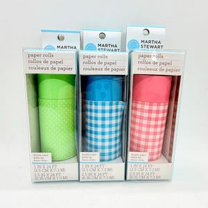 May include: Three Martha Stewart paper rolls in individual clear boxes. The left roll is green with white polka dots, the center is blue with a white gingham pattern, and the right is pink with a white gingham pattern. Each box lists 1 in x 24 ft.