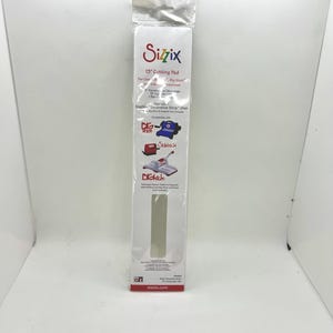 May include: A Sizzix 13-inch cutting pad in a clear plastic package. The package has the Sizzix logo and product information, including compatibility with Big Shot and Sidekick machines. The pad is designed for use with Sizzix Decorative Strip Dies.