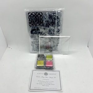May include: A clear stamp set featuring floral and decorative patterns, a transparent acrylic stamping block, and four small ink pads in green, pink, yellow, and brown. An instruction card labeled Anna Griffin Garden Party Clear Stamp Set is included.