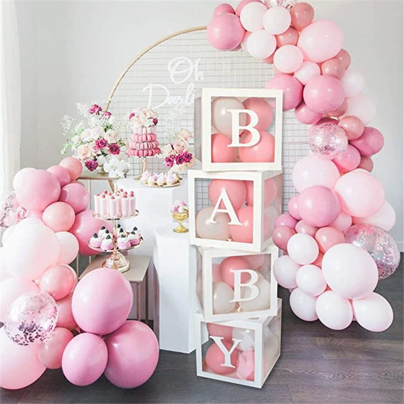May include: Four clear boxes stacked on top of each other, each box has a white border and a letter of the word "BABY" inside. The boxes are decorated with pink and white balloons.