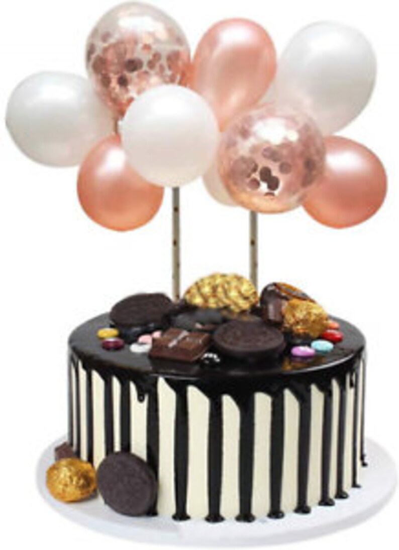 Pode incluir: Um bolo de chocolate com bal&otilde;es brancos e rosa dourado no topo. O bolo &eacute; decorado com raspas de chocolate, doces e um fio de chocolate.