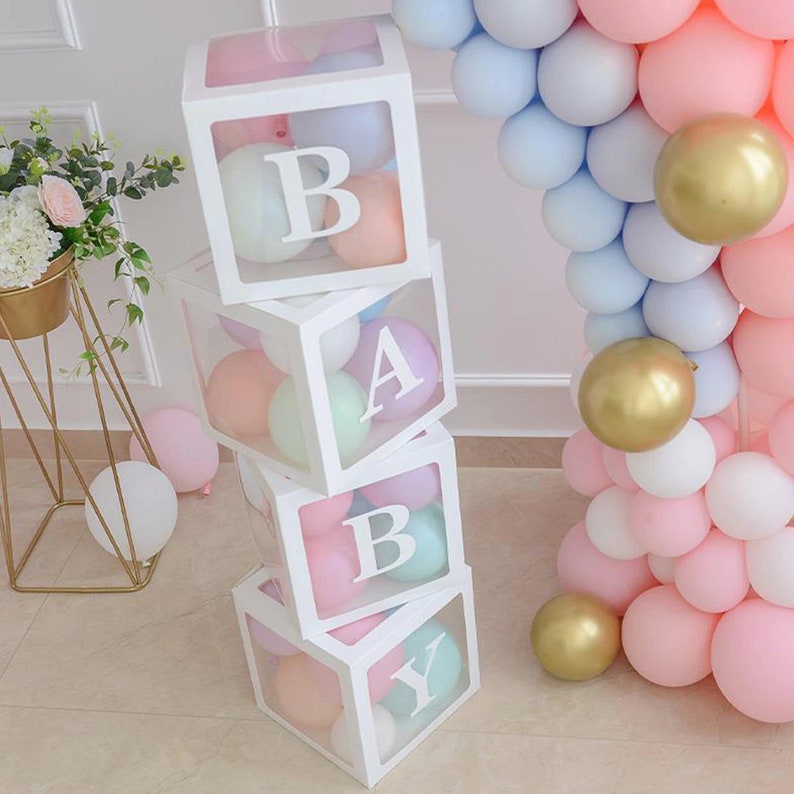 May include: A stack of four clear acrylic boxes with white frames, each containing pastel colored balloons. The boxes are stacked to spell out the word "BABY".