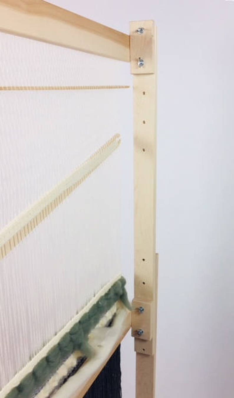 May include: A wooden loom with a white warp and a green weft. The loom is set up for weaving and has a wooden frame with a metal tensioning system.
