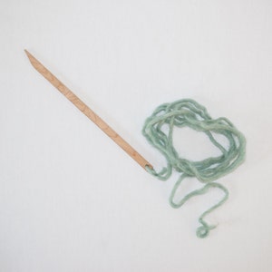 Peut inclure: Une aiguille en bois avec un trou &agrave; l'extr&eacute;mit&eacute; et une pelote de fil vert clair.