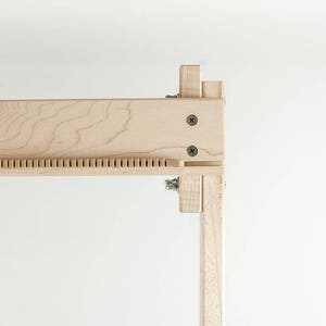 May include: Close-up of a wooden frame with a series of small holes along the top edge. The frame is made of light-colored wood and has a natural finish.