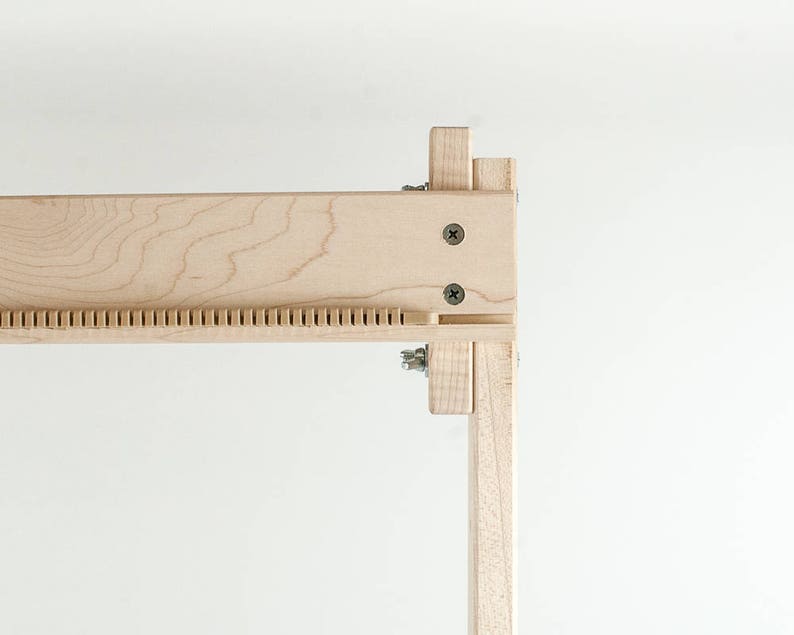 May include: Close-up of a wooden frame with a series of small holes along the top edge. The frame is made of light-colored wood and has a natural finish.