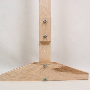 May include: A wooden easel stand with a wide base and adjustable height. The stand is made of natural wood and has a simple design.