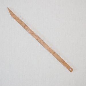 Peut inclure: Un long et fin cheveu en bois avec une pointe pointue et un petit trou &agrave; l'autre extr&eacute;mit&eacute;. Le cheveu est brun clair avec un grain de bois naturel.