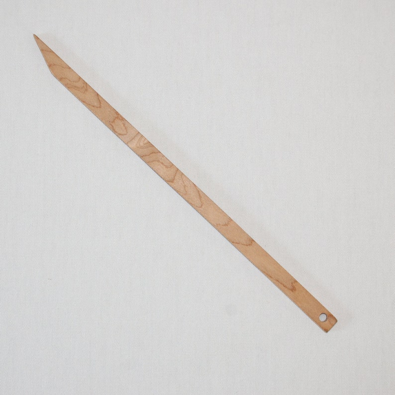 Peut inclure: Un long et fin cheveu en bois avec une pointe pointue et un petit trou &agrave; l'autre extr&eacute;mit&eacute;. Le cheveu est brun clair avec un grain de bois naturel.