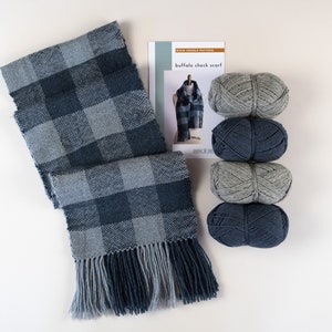 May include: A knitting kit for a buffalo check scarf. The kit includes four skeins of yarn in shades of gray and blue, and a pattern for the scarf. The scarf is already knitted and is shown in the image.