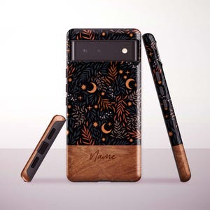 Puede incluir: Funda de teléfono con fondo negro con un patrón celestial de estrellas, lunas crecientes y follaje en naranja y azul. La parte inferior es un diseño de vetas de madera con la palabra "Name" en escritura.