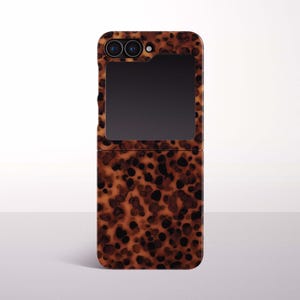 May include: A foldable smartphone case featuring a brown and black tortoiseshell pattern. The case has a rectangular cutout at the top for the camera lenses and a secondary display screen, with a hinge mechanism visible in the middle of the body.