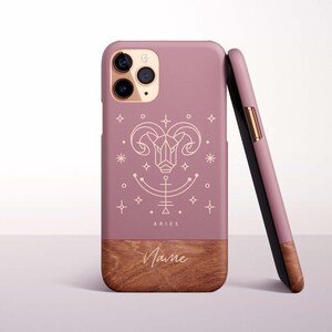 Puede incluir: Funda de teléfono malva con base de vetas de madera. La funda presenta un símbolo del zodiaco Aries blanco y la palabra "ARIES". La parte inferior tiene espacio para un nombre en fuente de escritura.