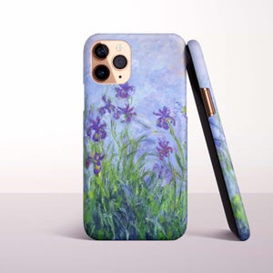 May include: A smartphone case featuring an impressionist-style painting of purple irises and green foliage against a light blue background. The case has a cutout for a triple-lens camera system and a slim profile with a metallic side button detail.
