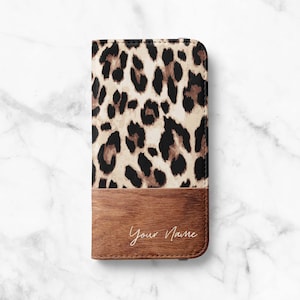 May include: A phone case with a leopard print pattern on the top half and a wood-grain design on the bottom. The words "Your Name" are written in cursive on the wood-grain section. The case is rectangular and appears to be made of leather or a similar material.