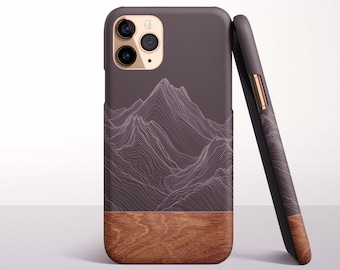 May include: A phone case with a mountain design. The top portion of the case is a dark gray color with a white mountain range design. The bottom portion of the case is a wood grain design. The case is leaning against another case.