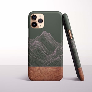 May include: A dark green phone case with a mountain range design in pink lines. The bottom half of the case is a wood grain pattern. A second case is leaning against the first.