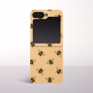 Puede incluir: Funda de teléfono beige con un patrón repetido de abejas ilustradas en amarillo y negro. La funda tiene un área de pantalla negra rectangular y un módulo de cámara en la parte superior.