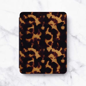 Peut inclure: Un étui rectangulaire pour liseuse électronique arborant un motif écaille de tortue dans des tons brun foncé et ambre. La couverture de protection présente des coins arrondis et une finition lisse et uniforme sur toute la surface.