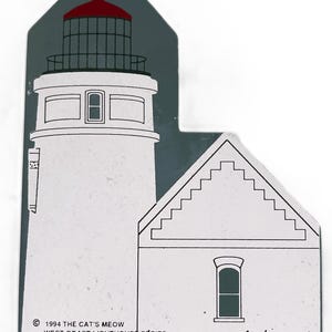 Puede incluir: Objeto decorativo de madera con forma de faro. El faro es blanco con la parte superior roja y un fondo gris oscuro. El texto dice "1994 The Cat's Meow West Coast Lighthouse Series Heceta Head Light".