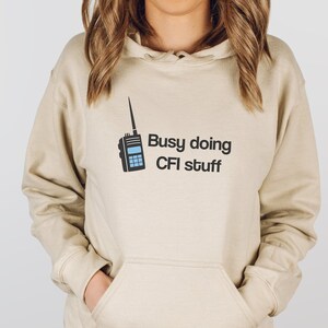 May include: A beige hoodie with a black graphic of a walkie-talkie and the text "Busy doing CFI stuff".