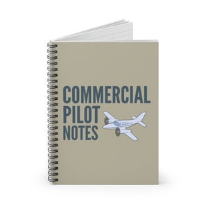 Op de afbeelding: Spiraalgebonden notitieboek met de tekst "COMMERCIAL PILOT NOTES" in donkerblauw. Een lichtblauwe vliegtuigafbeelding staat naast de tekst. Het notitieboek heeft een bruinachtige kaft en witte gelinieerde pagina's.
