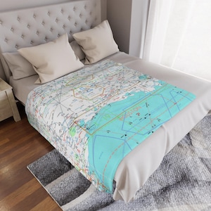 May include: A white bed with a light blue and white map printed throw blanket. The map shows the Houston area with roads and highways.