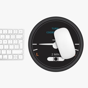 Puede incluir: Alfombrilla de ratón redonda negra con un diseño de panel de instrumentos de avión blanco. El panel tiene el texto "TURN COORD" y "2 MIN.". La aguja apunta hacia la izquierda.