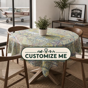 May include: A round tablecloth featuring a detailed aeronautical sectional chart print with yellow, blue, and white topographic lines and navigation markers. The fabric is draped over a circular wooden table with a potted green plant in the center.