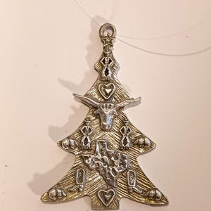 May include: A silver-toned metal Christmas tree ornament featuring a textured background. The design includes a longhorn steer head, a map of Texas, cowboy boots, armadillos, hearts, and a star at the top. A clear hanging loop is attached.