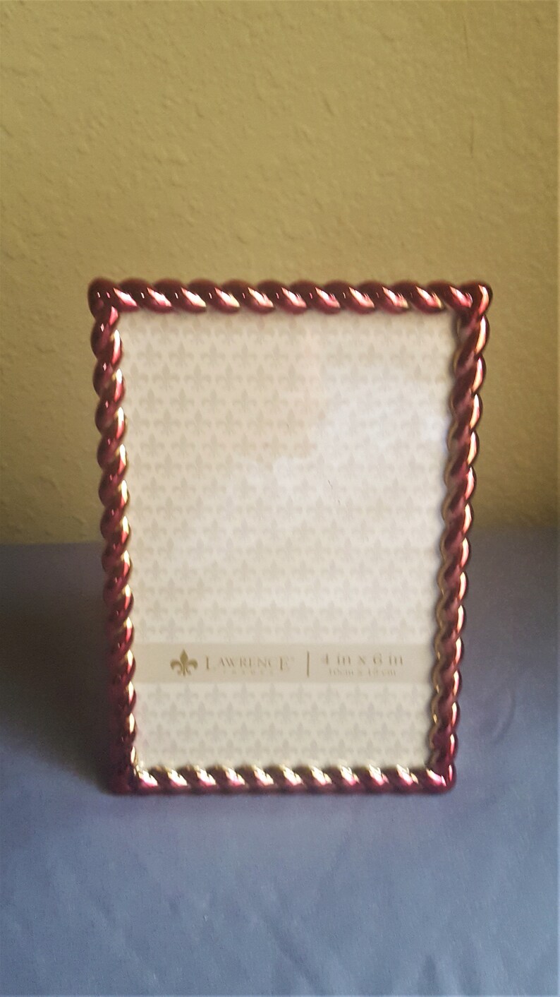 May include: A red and gold picture frame with a rope-like design around the edge. The frame is 4 inches by 6 inches and is made by Lawrence & Co.