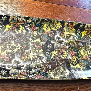 May include: A vintage, rectangular serving tray with a yellow, black, and green floral pattern. The tray is made of plastic and has a glossy finish.