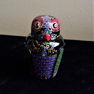 May include: A black painted wooden owl figurine with colorful details. The owl has red, yellow, and blue eyes, a red beak, and purple and green feathers.