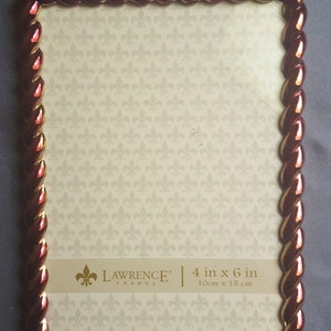 May include: A red and gold picture frame with a rope-like design. The frame is 4 inches by 6 inches and is made by Lawrence Frames.