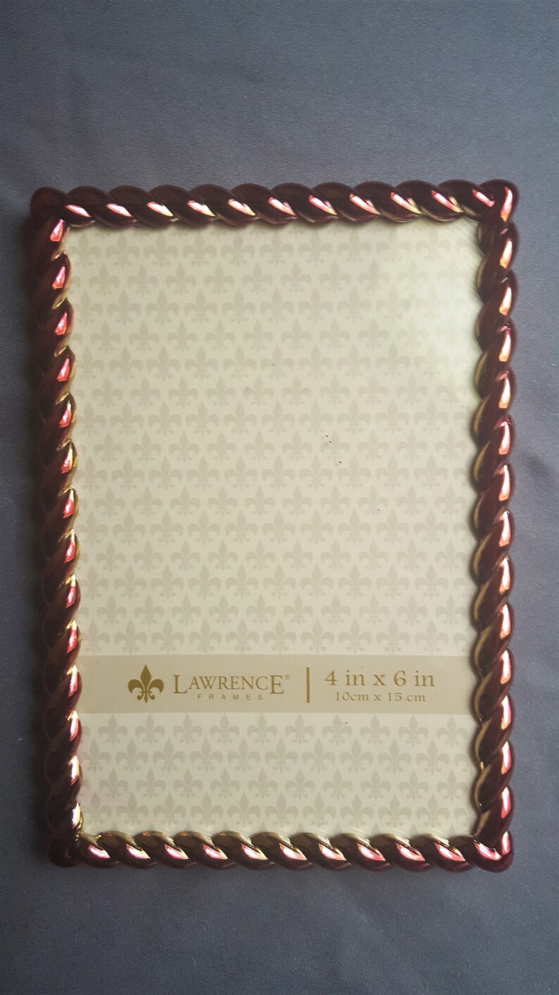 May include: A red and gold picture frame with a rope-like design. The frame is 4 inches by 6 inches and is made by Lawrence Frames.