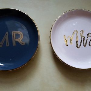 May include: Two ceramic ring dishes, one blue with gold trim and the word "MR" in gold lettering, the other pink with gold trim and the word "Mrs" in gold lettering.