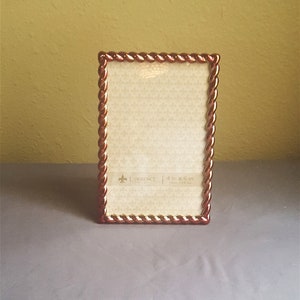 May include: A gold and red picture frame with a rope-like design around the edge. The frame is 4 inches by 6 inches and has a white mat.