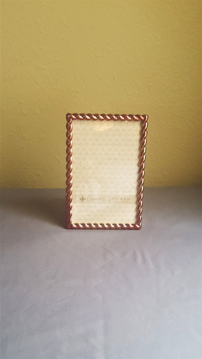 May include: A gold and red picture frame with a rope-like design around the edge. The frame is 4 inches by 6 inches and has a white mat.