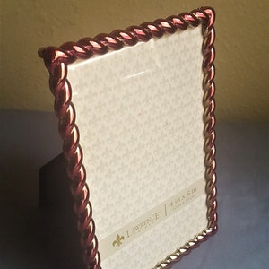 May include: A red and gold picture frame with a rope-like design. The frame is 4 inches by 6 inches and is made by Lawrence Frames.