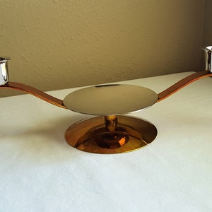 May include: A silver and gold candle holder with two candle cups and a round base. The holder has a curved design.